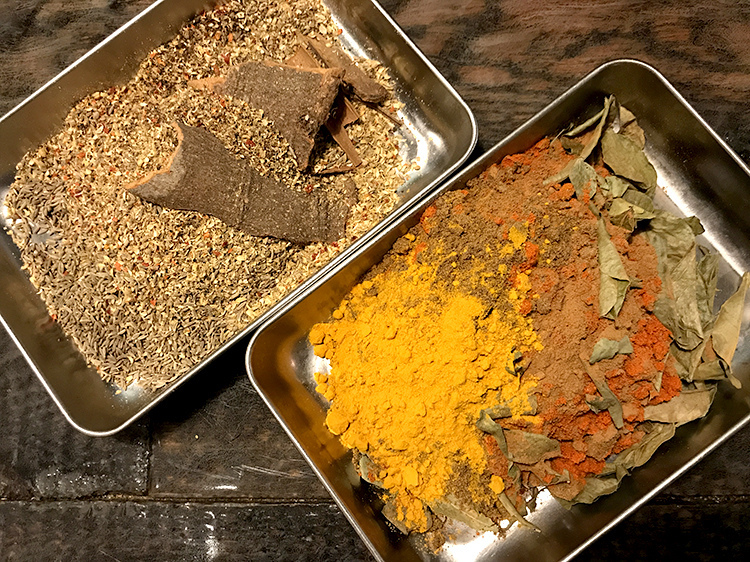ターメリックやチリパウダーなど辛味と風味が効いたオリジナルのガラムマサラ（右）と、カオスキーマに使うスパイスの数々（左）