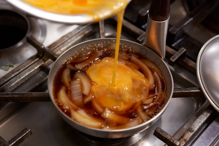 親子丼用の小鍋に出汁とスライスした玉ねぎを入れ、さっと煮る。ここに伊達鷄の溶き卵二個分を入れ、蓋をしてひと煮たちさせる。このだしと卵の量もポイント