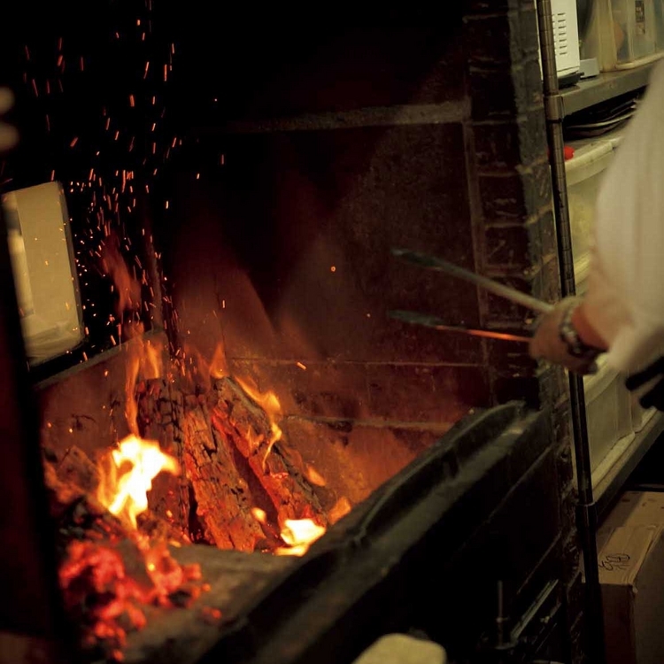 耐火煉瓦で特注されたトスカーナ暖炉。右側で薪を焚いて炭化させて熾火をつくり、左手前のグリルの網の下に熾火を仕込んで肉を焼く
